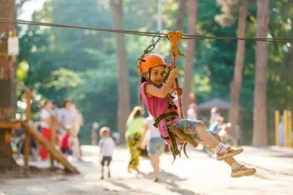 Happy school girl enjoying activity in a climbing adventure park on a summer day